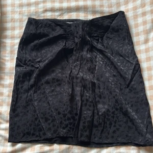 Svart kjol med hjärtmönster & Other Stories - Supersnygg svart kortkjol från & Other Stories Paris Atelier med subtilt hjärtmönster i tyget. Kjolen har en knytning framtill som ger en cool twist och är tillverkad i ett glansigt, mjukt material som känns lyxigt.