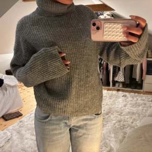 Grå ribbad polotröja - Mysig grå polotröja med ribbad struktur och oversized passform. Tröjan har hög polokrage och långa ärmar med breda muddar. Perfekt för kyliga dagar och enkel att styla med jeans eller kjol.