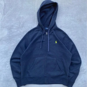 Polo Ralph Lauren zip hoodie - Snygg mörkblå hoodie i XS från Polo Ralph Lauren med dragkedja och huva. Tröjan har snörning i huvan och den klassiska gula broderade loggan på bröstet. Perfekt för en chill och stilren look.