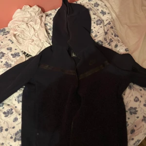 Svart Nike hoodie med dragkedja S - Svart hoodie från Nike i storlek S med hel dragkedja och huva. Snygga svarta detaljer över bröstet och diskret Nike-logga på vänster sida. Perfekt för chill dagar eller när du vill ha en sportig look.