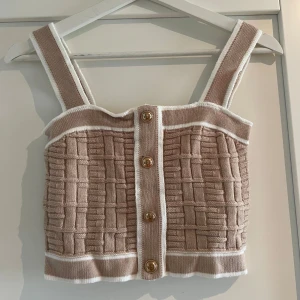 Beige stickad topp med knappar från SHEIN - Supersöt beige stickad linnetopp från SHEIN med vita kanter och snyggt rutigt strukturmönster. Toppen har breda axelband och guldiga knappar framtill som detalj. Croppad 