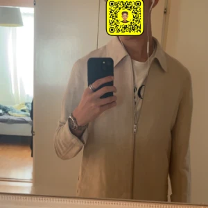 Beige overshirt från Lindbergh S - Snygg beige overshirt från Lindbergh i storlek S. Jackan har klassisk krage, raka linjer och dragkedja framtill. Materialet är linne och bomull, vilket ger en lätt och fräsch känsla. Perfekt att slänga på över en t-shirt för en clean look. Den har inte används en enda gång och taggen sitter till och med kvar. Kontakta gärna vid intresse😊