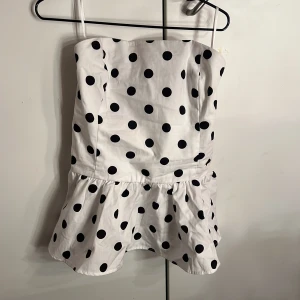 Vit prickig tubtopp från Bik Bok XS - Supersöt vit tubtopp med svarta prickar från Bik Bok. Har en volang nertill. Stretch material i bak. Endast testad, lappen är kvar.