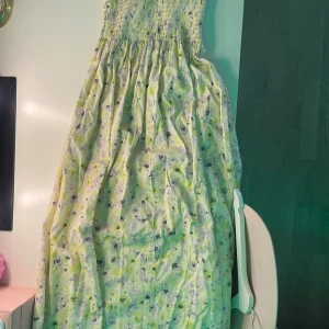 Ljusgrön blommig långklänning - Supersöt långklänning i ljusgrönt med blommigt mönster. Smockad upptill och utsvängd kjol som ger en flowy känsla. Perfekt för varma dagar och somriga vibes. Klänningen är ärmlös och har en romantisk look.