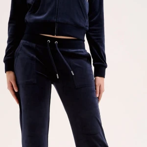 Mörkblå Juicy Couture sett - Säljer en mörkblå hoodie från Juicy Couture i mjuk velour. Tröjan har huva, dragkedja framtill och stora fickor. Perfekt för en chill look och riktigt skön att ha på sig. Klassisk logga broderad på bröstet och ribbade muddar vid ärmslut och midja.sytt byxorna Low Waist och de har lite lim fläckar på högra benet. Men om du är intresserad så kan ja skicka bild på defekterna!