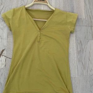Gul v-ringad topp med kort ärm - En enkel gul topp i bomull med v-ringning och korta ärmar. Modellen är rak och passar perfekt till jeans eller kjol. Toppen har en liten knappdetalj vid halsringningen för extra stil.