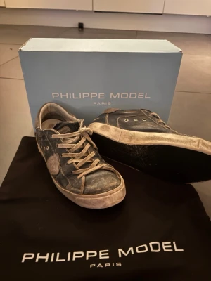 Philippe Model svarta  - Säljer ett par svarta Philippe Model sneakers i skinn med beige detaljer och vita snören. Skorna har rund tå, platt sula och metallöljetter på sidan. Klassisk streetstil med logotyp på sidan och kontrastsömmar. Kommer med originalkartong och dustbag.