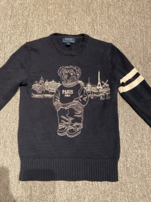 Mörkblå stickad tröja Polo Ralph Lauren - Nu säljs en blå stickad tröja med en björn och byggnader bakom björnen, nypris 1500