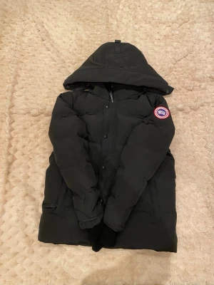 Svart Canada Goose dunjacka M - Dm för kvitto☺️Säljer en svart dunjacka från Canada Goose med huva och klassisk logga på ärmen. Jackan har dragkedja och knappar framtill, samt praktiska innerremmar för att bära den som ryggsäck. Perfekt för kalla vinterdagar och riktigt snygg streetstil.