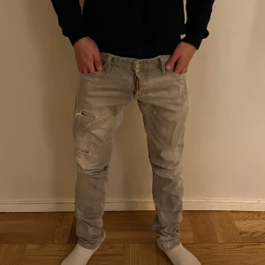 Grå slitna jeans från Dsquared 2 - Säljer ett par fräsha grå jeans från Dsquared 2  med slitningar och trasiga detaljer på framsidan. Modellen har en smal passform och klassisk femficksdesign. Skriv för minsta fundering!!