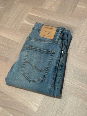 Jack& jones jeans Glenn - Säljer ett par jeans från Jack & Jones. Jeansen har en ljus tvätt och bruna detaljer på bakfickan samt en läderpatch med logga i midjan. Perfekt passform och stilren look. Modellen heter Glenn och är slim fit. Hör av dig vid funderingar! 