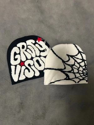 GRVTY VISION mössa den vita e no brand - Två mössor som är perfekta under vintern. Den svarta har en text på sig där det står GRvTY VISION den vita har ingen text bara spindelnät. Den vita har även en liten grå fläck. Sälja ej styckvis!