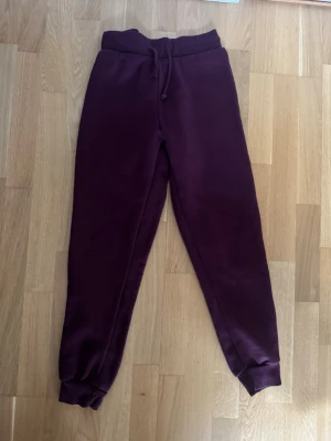 Mörklila mjukisbyxor med snörning - Säljer ett par mörklila mjukisbyxor med ribbade muddar vid bensluten och midja. Byxorna har snörning i midjan för extra komfort och är gjorda i mjukt material som passar perfekt för chill dagar. Snygg och enkel design utan synliga loggor.