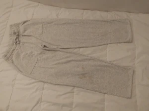 Grå mjukisbyxor med snörning - Säljer ett par ljusgrå mjukisbyxor med elastisk midja och snörning. Byxorna har sidofickor och är tillverkade i mjukt bomullsmaterial. Perfekta för chill hemma eller träning. Klassisk loose passform och enkel design.har en liten fläck som man set nät man kommer nära