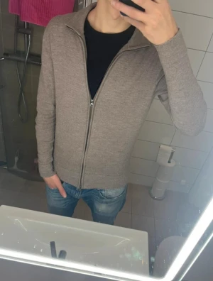 Beige full zip Selected Homme - Säljer en stilren beige kofta med dragkedja och hög krage. Nypris 1100kr. Koftan är långärmad och har en normal passform, perfekt att slänga på över en t-shirt. Materialet känns mjukt och är stickat, vilket gör den skön att bära under kyligare dagar. Storlek L men har krympt så den passar mer som M/S 