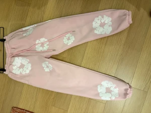 Rosa mjukisbyxor från Denim Tears - Inköpt i New York. Säljer ett par rosa mjukisbyxor från Denim Tears med vita blommiga tryck över hela byxorna. Byxorna har elastisk midja med snörning och muddar vid bensluten. Materialet är mjukt och skönt, perfekt för chill dagar. Finns även fickor på sidorna och bak. 