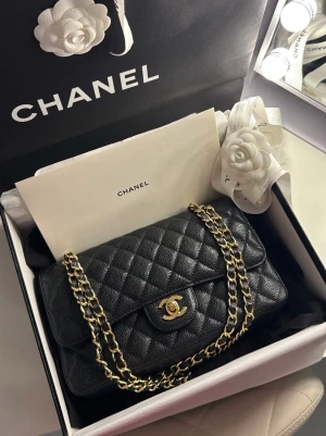 Chanel cc classic caviar quilted double flap bag 2021 - Säljer en ikonisk Chanel Classic Medium Double Flap från 2021 i svart caviar-läder med röd insida och guldfärgad hårdvara. Den tidlösa quiltningen och det klassiska CC-låset gör väskan lika självklar till vardags som vid mer formella tillfällen.  Väskan är köpt via Vinted med verifikation. Den säljs med originalkvitto, box, dustbag samt övriga originaltillbehör.  Väskan har aldrig använts efter köpet då storleken tyvärr inte passar mig. Skicket är mycket fint, nästintill nyskick. Det finns endas