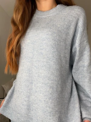 Ljusblå stickad tröja med loose fit - Mysig ljusblå stickad tröja med rund hals och lång ärm. Tröjan har en loose passform och är tillverkad i ett mjukt stickat material som känns skönt mot huden. Perfekt för kyliga dagar och enkel att matcha med jeans eller leggings.