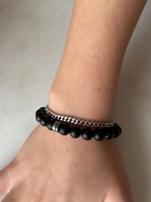 Svart pärlarmband med silverdetalj - Stilrent svart armband med matta pärlor och en cool silverfärgad detalj. Perfekt att kombinera med andra smycken för en personlig look. Elastiskt band gör det enkelt att ta på och av. Passar dig som gillar minimalistisk och modern stil.