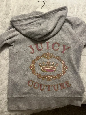Juicy couture zip up hoodie - Grå zip up hoodie med guld/rosa design på ryggen. En liten fläck på sidan av ryggen, se sista bild. Pris kan diskuteras. 