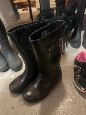 Svarta McKinley stövlar EU35 - Säljer ett par klassiska svarta stövlar från McKinley, modell Strada W. De är höga med rund tå och har ett spänne på sidan som detalj. Tillverkade i syntetmaterial och perfekta för regniga dagar eller promenader i stan.