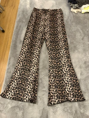 Leopardmönstrade vida byxor Luca & Lola - Säljer ett par riktigt snygga leopardmönstrade byxor från Luca & Lola i storlek L. De är vida i modellen, har resår i midjan och är gjorda i ett mjukt, stretchigt syntetmaterial. Perfekta för dig som vill sticka ut med ett djurmönster och gillar bekväma, flowiga byxor.