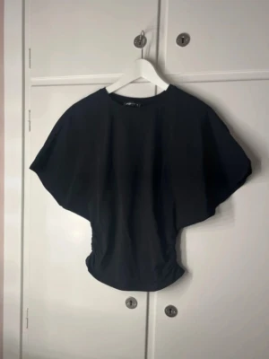 Svart croppad topp från FB Sister - Säljer en svart croppad topp från FB Sister med breda, nästan fladdermusliknande ärmar och rund halsringning. Toppen har en loose passform och är tillverkad i mjuk bomull, perfekt till jeans eller kjol.