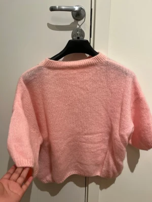 Ljusrosa stickad trekvarts tröja - Supermjuk och fluffig ljusrosa stickad tröja med kort, oversized passform och trekvarts ärmar. Perfekt till både jeans och kjol för en chill och söt look. Rund halsringning och loose fit gör den extra bekväm.