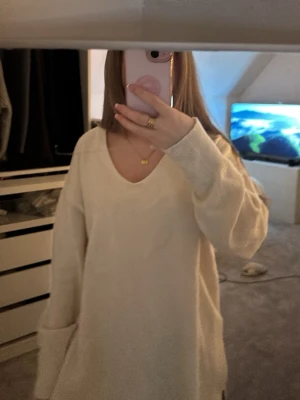 Beige stickad tröja från H&M - Mysig beige stickad tröja från H&M med v-ringning och långa ärmar. Tröjan har ribbade muddar och slits i sidorna för en avslappnad look. Perfekt för lager på lager under höst och vinter.
