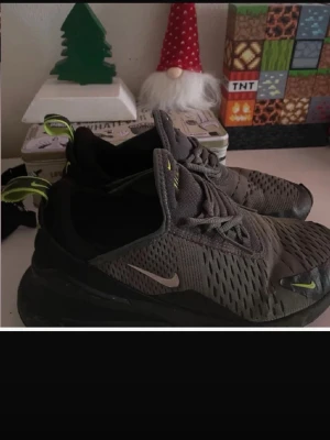Nike Air Max 270 sneakers grå/gul - Säljer ett par Nike Air Max 270 sneakers i grått med neongula detaljer och svart sula. Skorna har ventilerande mesh-ovandel, snörning och tydlig Air-dämpning i hälen. Perfekta för dig som vill ha en sportig och modern look. Med små hål där fram 