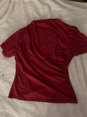 Vinröd kortärmad topp - Säljer en enkel och snygg vinröd topp med korta ärmar. Toppen har en lätt figurnära passform och är gjord i mjukt bomullsmaterial. Perfekt till jeans eller kjol för en clean look.
