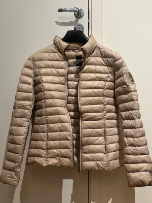 Beige pufferjacka från 48 7 Sweden - Säljer en beige pufferjacka från 48 7 Sweden i storlek S. Jackan har quiltad design, hög krage och dragkedja framtill. Märkets patch sitter på ena ärmen och jackan är lätt och smidig, perfekt för kyliga dagar till hösten eller våren. 