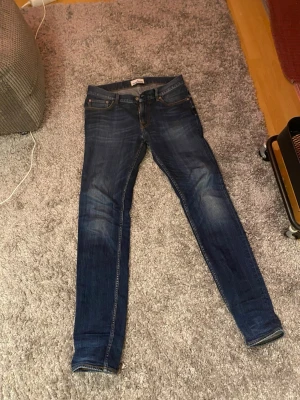 Stone Island blå  jeans 30/34 - Säljer ett par mörkblå jeans från Stone Island med klassisk patch på bakfickan. Jeansen har orange kontrastsömmar, fem fickor och dragkedja. Tillverkade i slitstarkt denim med snygga slitningar och tvättade detaljer för en cool look.