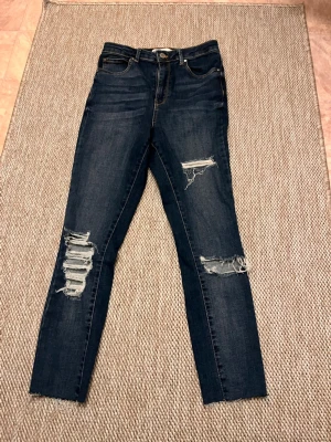Mörkblå skinny jeans med slitningar - Säljer ett par mörkblå skinny jeans med hög midja och snygga slitningar över knäna. Hela jeansens läng är 88 cm!😊