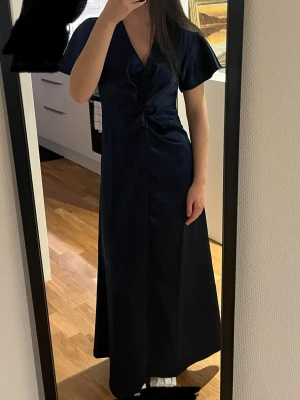 Marinblå långklänning i satin - Säljer en elegant marinblå långklänning i glansigt satinliknande material. Klänningen har v-ringning, korta vida ärmar och en snygg twist-detalj framtill i midjan. Passformen är normal och modellen faller snyggt längs kroppen. Köpt för 600kr och säljer för 400kr med prislapp kvar 😍