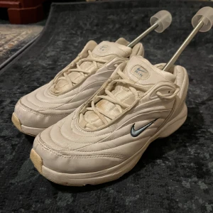 Nike Air vita retro sneakers - Nike Air sneakers i retrostil med vit ovandel i skinn och syntet. Snygga vågformade sömmar, klassisk Nike Swoosh i silver på sidan och robust sula med mönstrad undersida. Skorna har snörning och en chunky siluett som sticker ut.