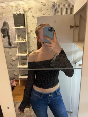 Leopardmönstrad offshoulder topp - Säljer en snygg offshoulder topp med leopardmönster i svart och brunt. Toppen är croppad och har långa, lätt transparenta ärmar med vågig kant. Endast använd en gång 
