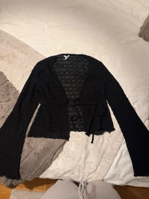 Svart spetskofta från Amisu - Säljer en svart, transparent spetskofta från Amisu i storlek M. Koftan har långa ärmar, knytband i midjan och ett snyggt spetsmönster som ger en luftig och trendig look. Perfekt att slänga över ett linne eller topp för extra stilpoäng.