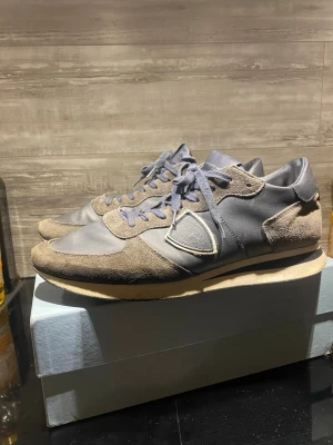 Philippe Model skor - Snygga sneakers från Philippe Model i en mörkblå färg med detaljer i mocka och släta partier i skinn. Skorna har snörning, rund tå och en svart sula. Klassisk logga på sidan och bekväm innersula. Perfekta för dig som gillar stilrena och exklusiva sneakers. Tyvärr har dom en liten röd fläck på sidan. Pris inte hugget i sten