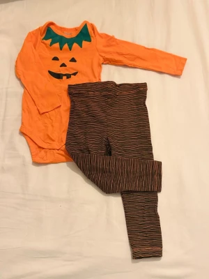 Pumpa-body och randiga byxor Lupilu - Säljer ett gulligt set från Lupilu med orange långärmad body med pumpatryck och gröna detaljer vid halsen. Tillhörande byxor är bruna med tunna orange ränder. Perfekt till halloween eller temadagar!