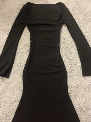 Svart långärmad klänning - Säljer en svart långärmad klänning från SHEIN med fyrkantig ringning och figurnära passform. Klänningen har långa, lätt utsvängda ärmar och är sydd i ett mjukt, stretchigt material som ger en snygg siluett. Perfekt för dig som gillar minimalistisk och stilren look. Aldrog använt och har haft den i ett år. 