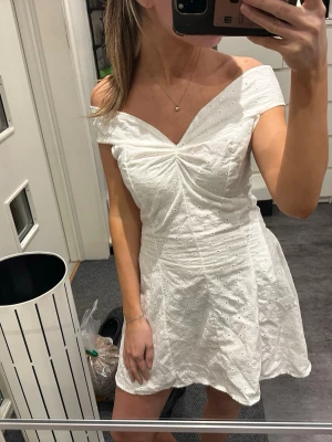 Vit offshoulder kortklänning - Supersöt vit kortklänning med offshoulder och v-ringad urringning. Klänningen har broderade detaljer och lätt utställd kjol som ger en romantisk vibe. Perfekt för sommarens alla tillfällen!