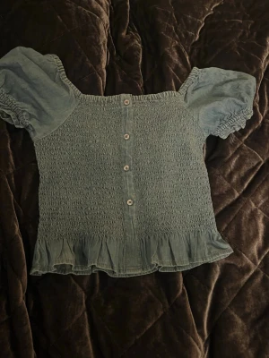 Blå blus med puffärm från KappAhl - Supersöt blå blus från KappAhl i storlek 146. Tröjan har puffärmar och smock över hela kroppen. Knappdetaljer framtill och volangkant nedtill. Funderingar? Skriv till mig💕