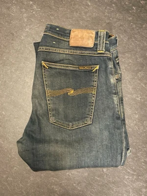 Nudie Jeans  - Säljer ett par blåa jeans från Nudie Jeans     (Grim Tim), storlek W31/L34, slim fit. Mycket bekväma jeans och är lite stretchiga. Mycket fint skick där de använts fåtal gånger.                                                     Nypris 1600kr                                                         Mått: A=42cm B=85cm C=112cm D=18cm       Fråga gärna om fler bilder eller om det är något ni generellt undrar!                                                    Checka in profilen för liknande jeans!