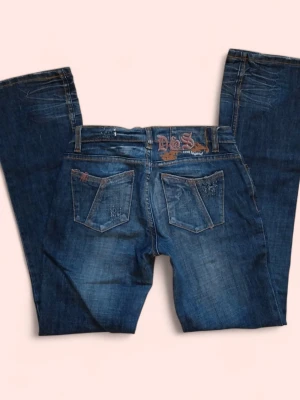 Lågmidjade bootcut jeans - Coola jeans från Colours Of The World. Storlek 34. Midjemått: 37cm. Innerbensmått: 81cm. 78% bomull. Tjockt & bra matreal. Broderad design på bakfickan.