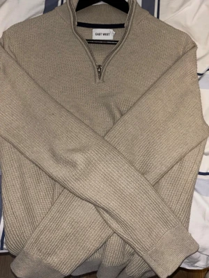 Beige stickad quarterzip - Säljer en beige stickad tröja från East West i 100% bomull. Tröjan har half zip-dragkedja, ribbade muddar och långa ärmar. Extremt bra passform och tillverkad av skönt material. Tyvärr behöver jag sälja vidare den så jag sorgligt nog växt ur den..