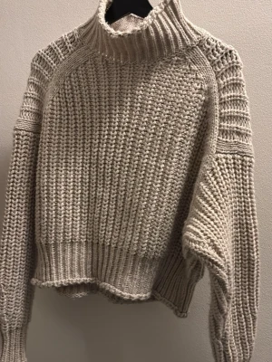 Beige stickad polotröja - Säljer en  beige stickad halvpolotröja med bred ribbad krage och långa ärmar. Tröjan har en oversized passform och grovstickad struktur som ger en riktigt mysig vibe. 