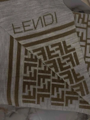 Beige stickad väst med mönster från Fendi - Säljer en beige stickad väst från Fendi med ikoniskt geometriskt mönster i brunt och diskret logga upptill. Västen har raka linjer och är tillverkad i mjukt material som ger en lyxig känsla. Perfekt för dig som vill ha något stilrent men ändå sticker ut.