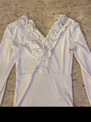 Vit spetsdetaljerad topp Gina Tricot - Supersnygg vit topp från Gina Tricot i storlek XS. Toppen har långa ärmar och v-ringning med breda spetsdetaljer längs urringningen. Materialet är mjukt och stretchigt, vilket gör den bekväm att bära. Perfekt för dig som gillar romantiska detaljer.