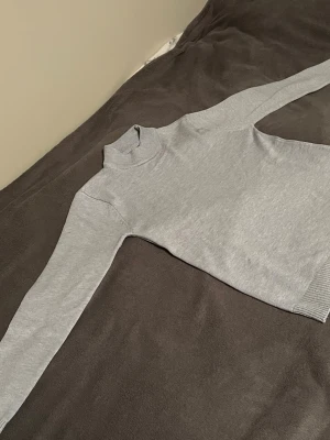 Ljusgrå polotröja i bomull - En stilren ljusgrå polotröja med lång ärm och ribbade muddar. Tröjan är tillverkad i mjuk bomull och har en klassisk passform som funkar till många olika looks. Perfekt för lager på lager under höst och vinter.